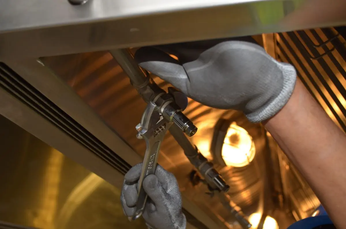A plumbing professional tightening a pipe valve with an adjustable wrench during a repair