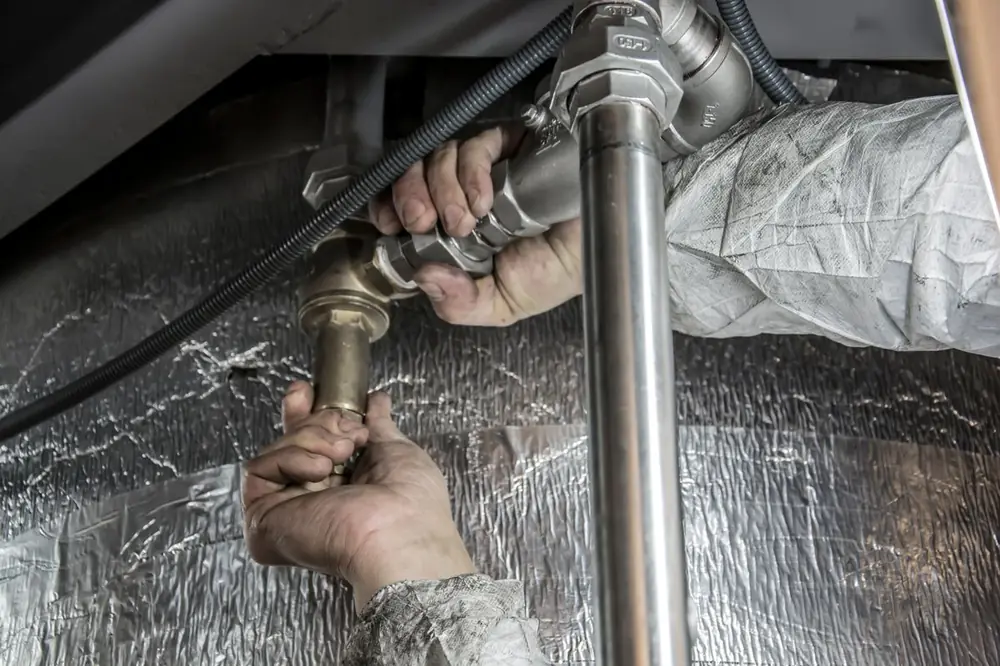 A plumbing professional's hands tightening a pipe fitting during a repair